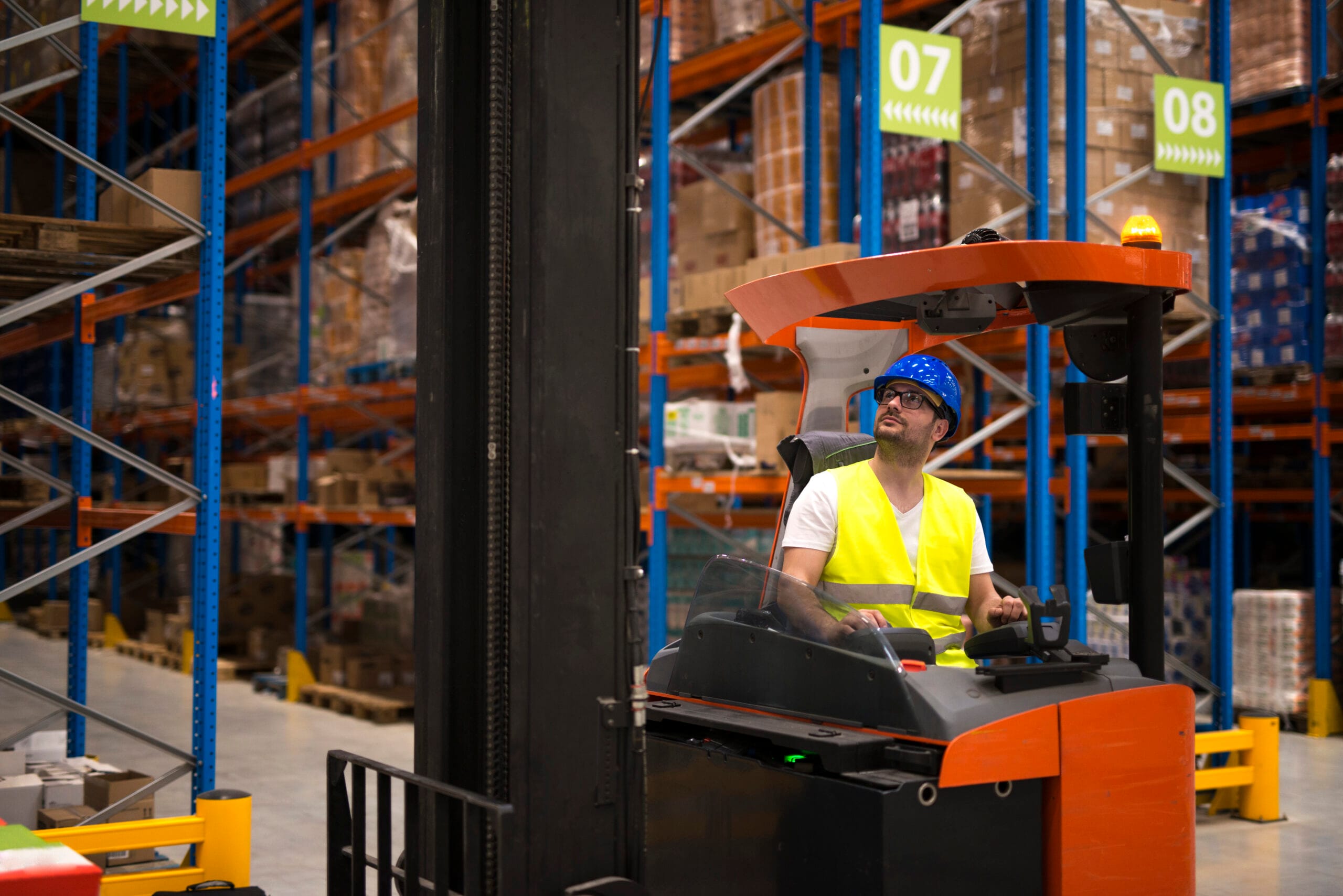 Forklift driver relocating and lifting goods in large warehouse ...